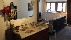 Ein Wohnzimmer mit einer Holzkommode, einem Spiegel, einer Vase mit roten Rosen, einem Glasbehälter und einem Sofa.