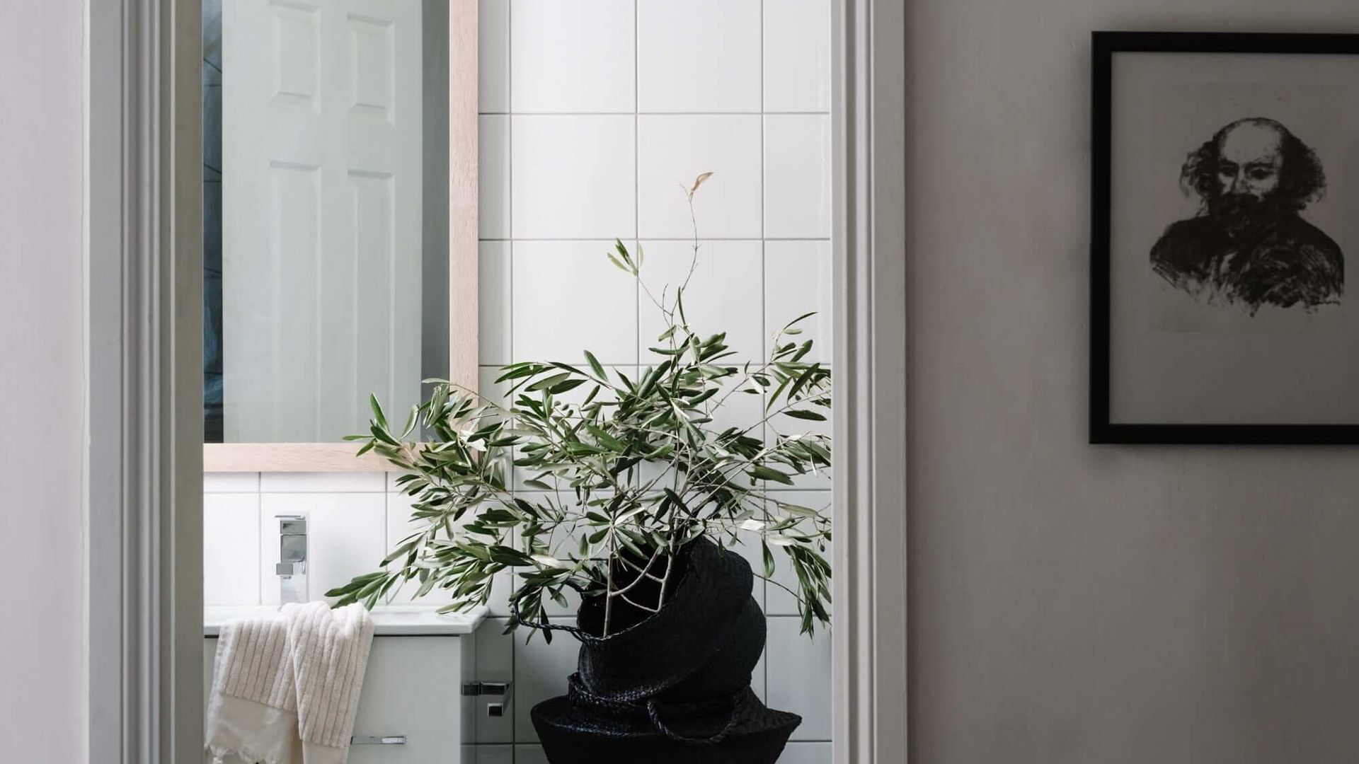 Um banheiro com uma planta em vaso, uma toalha e um quadro na parede.
