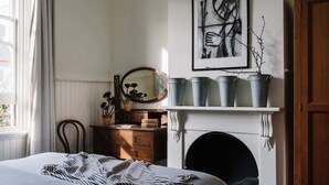 A bedroom with a bed, dresser, mirror, and a fireplace with pots on the mantel.