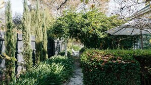 A garden pathway with a wooden fence, a white chair, and a pergola with a white umbrella.