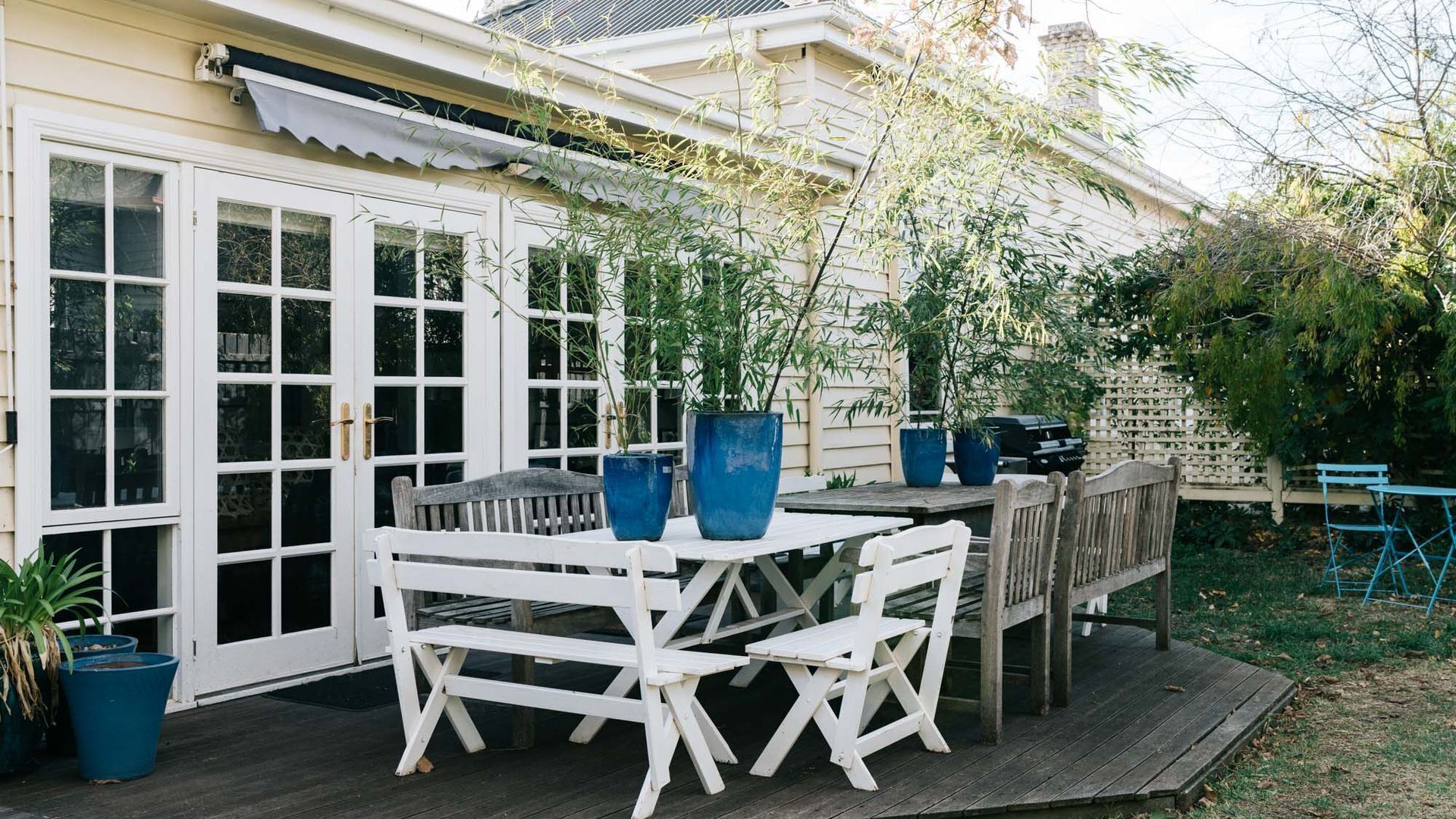 A wooden deck with a white table and chairs, surrounded by potted plants and a wooden fence.