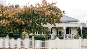 A white two-story house with a porch, surrounded by a white picket fence.