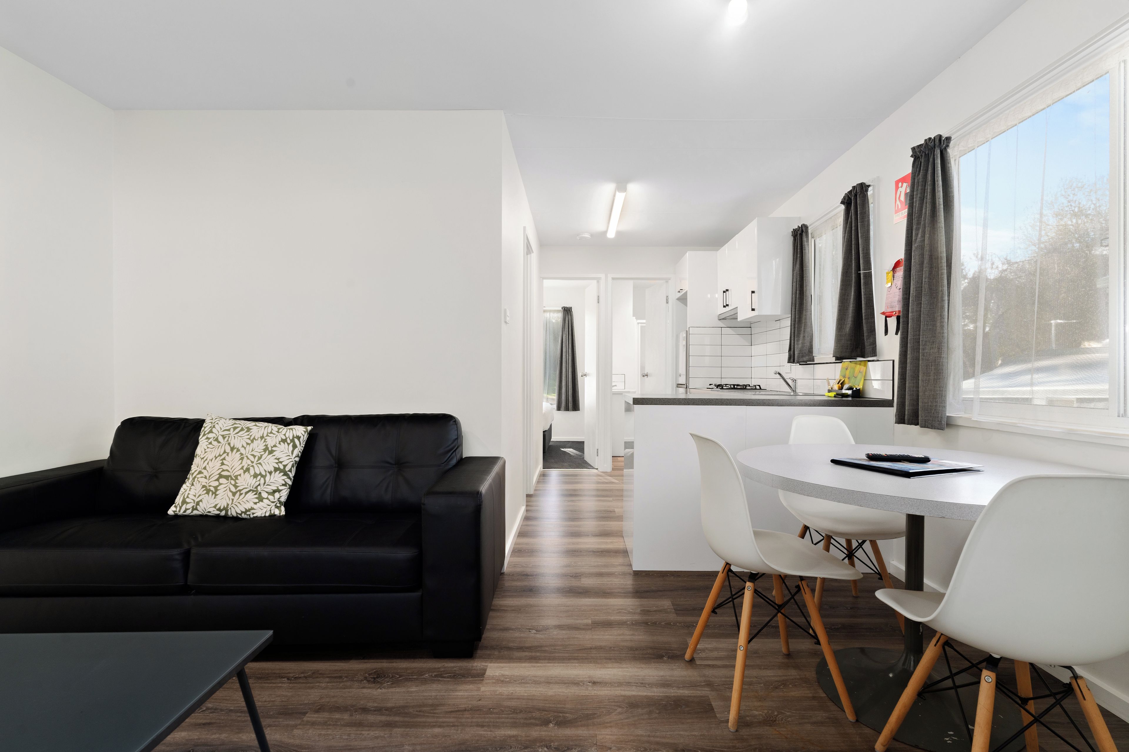 A modern living room with a black sofa and a dining area with a white table and chairs.