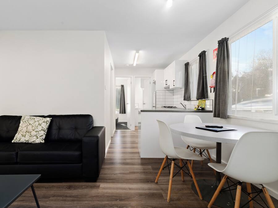 A modern living room with a black sofa and a dining area with a white table and chairs.