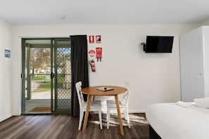 A hotel room with a bed, a TV mounted on the wall, a dining table with chairs, and a door leading outside. - BIG4 Tiny Away Stay – Seymour Riverside (Seymour)
