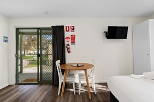 Habitación de hotel con cama, televisor montado en la pared, mesa de comedor con sillas y puerta que da al exterior.