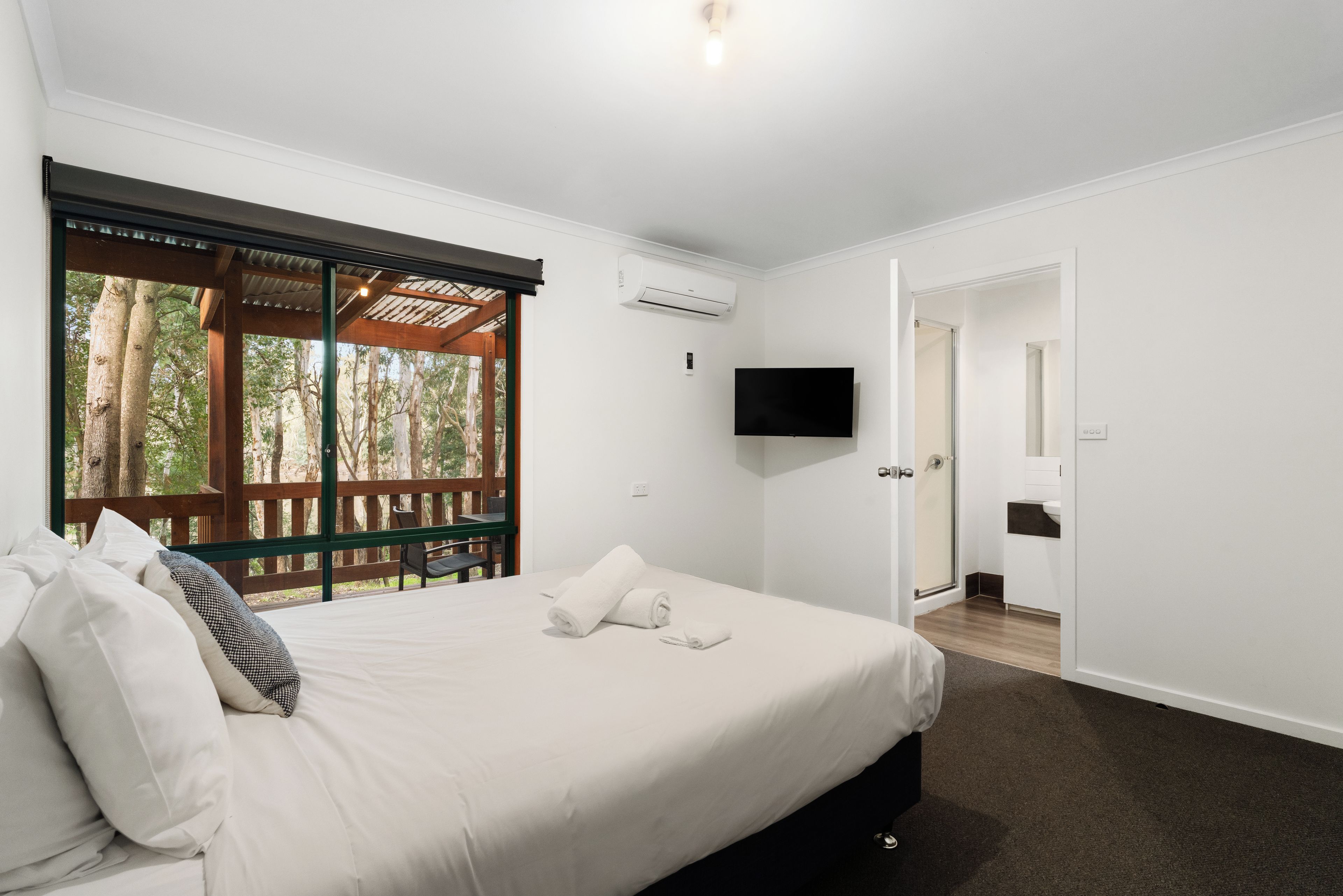Un dormitorio con cama, televisor, puerta y ventana con vista a árboles.