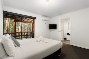 Ein Schlafzimmer mit einem Bett, einem Fernseher, einer Tür und einem Fenster mit Blick auf Bäume.