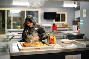 A person cooking at a buffet with a variety of condiments and plates on the counter. - BIG4 Tiny Away Stay – Seymour Riverside (Seymour)