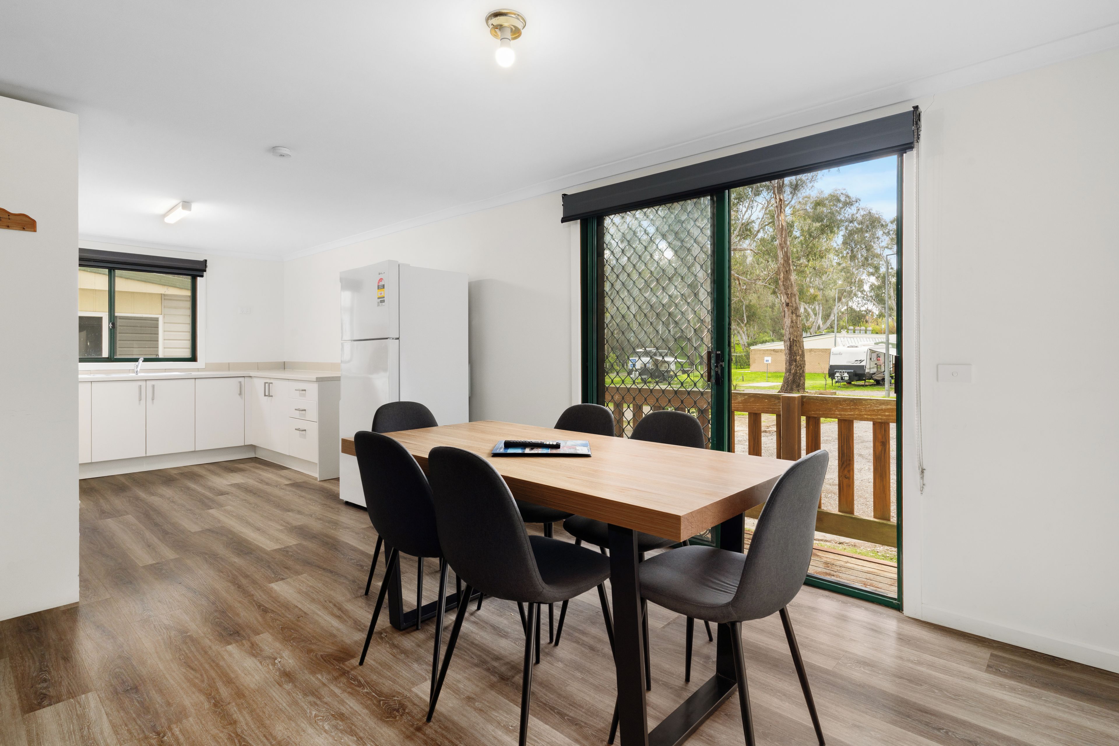 A modern kitchen with white cabinets, a refrigerator, and a dining area with a wooden table and black chairs.