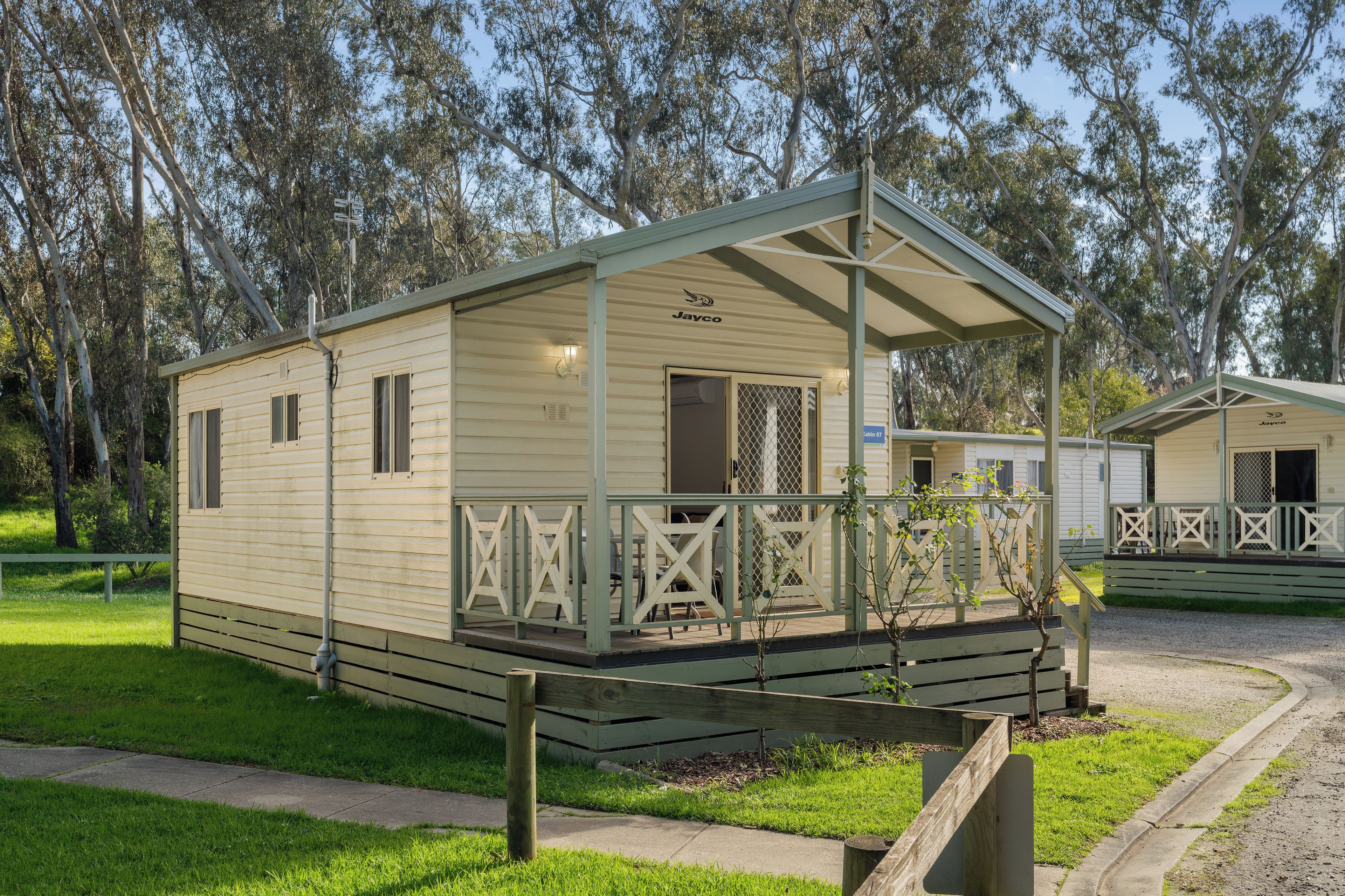 A small, single-story, light-colored mobile home with a porch and a fenced deck area.