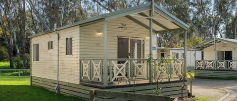 A small, single-story, light-colored mobile home with a porch and a fenced deck area.