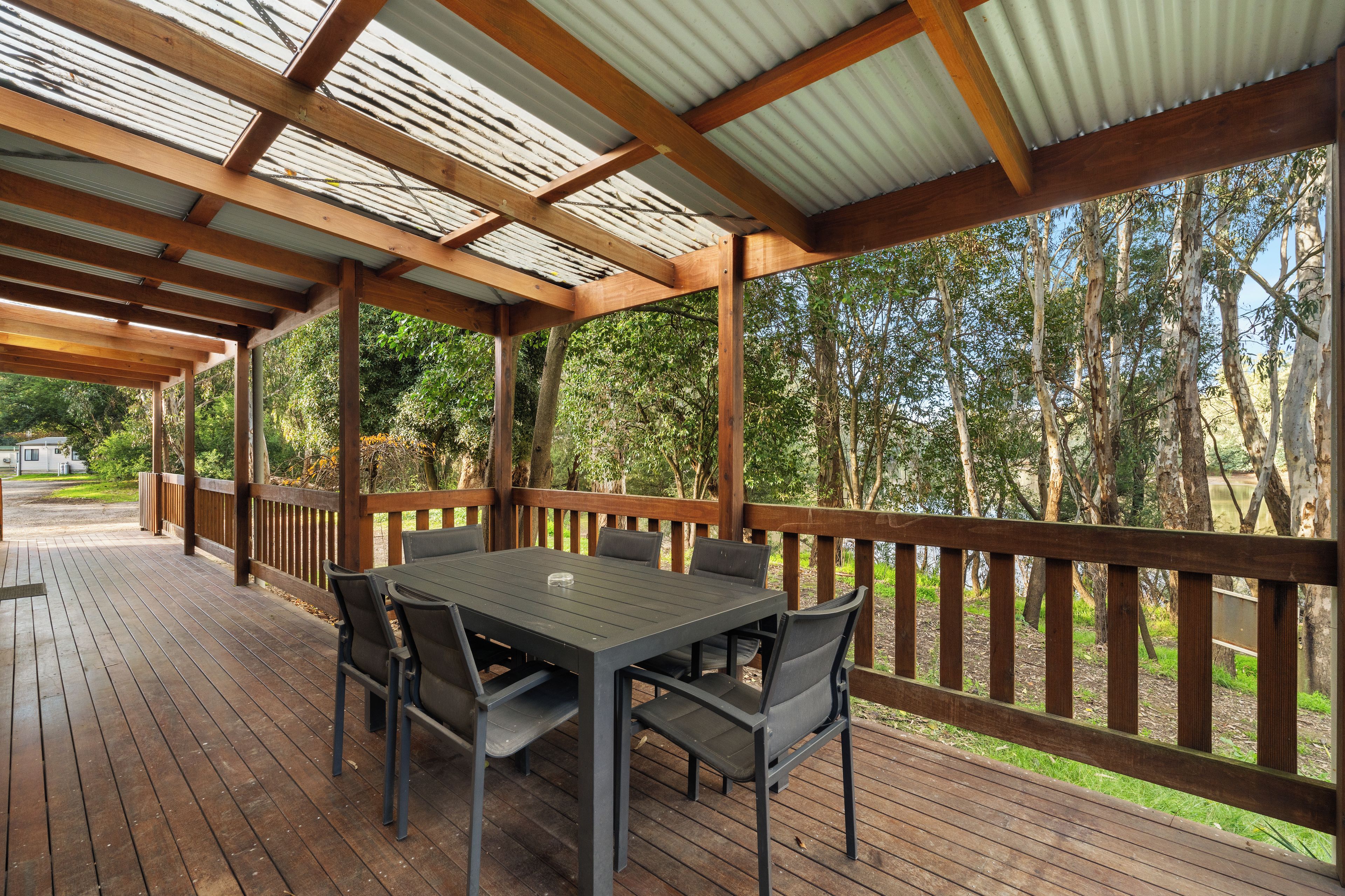 An outdoor covered patio with a table and chairs, surrounded by a wooden deck and a metal railing.