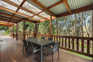 An outdoor covered patio with a table and chairs, surrounded by a wooden deck and a metal railing.