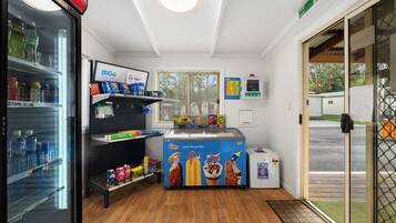 A small ice cream shop with a freezer, shelves stocked with snacks, and a window with blinds.