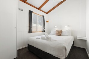 Ein Hotelzimmer mit einem Bett, einem Fenster mit Vorhängen, einem Nachttisch und einer Wandleuchte.