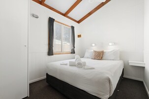 Habitación de hotel con cama, ventana con cortinas, mesita de noche y lámpara fijada a la pared.