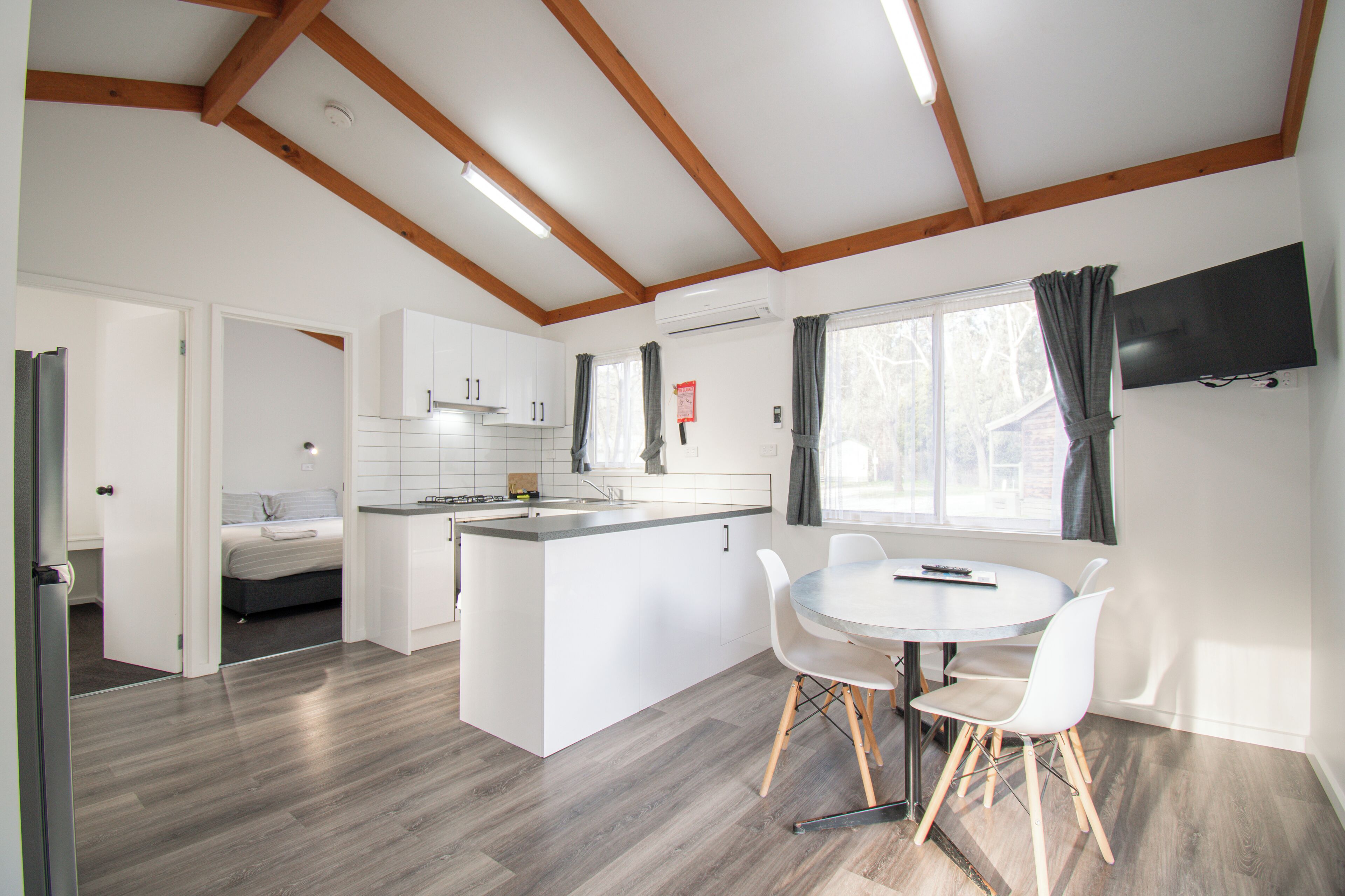 A modern kitchen with white cabinets, a central island, and a dining area with a round table and white chairs.