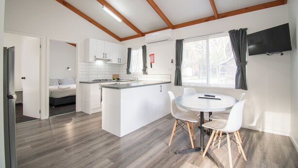 Une cuisine moderne avec des meubles blancs, un îlot central et un coin repas comprenant une table ronde et des chaises blanches.