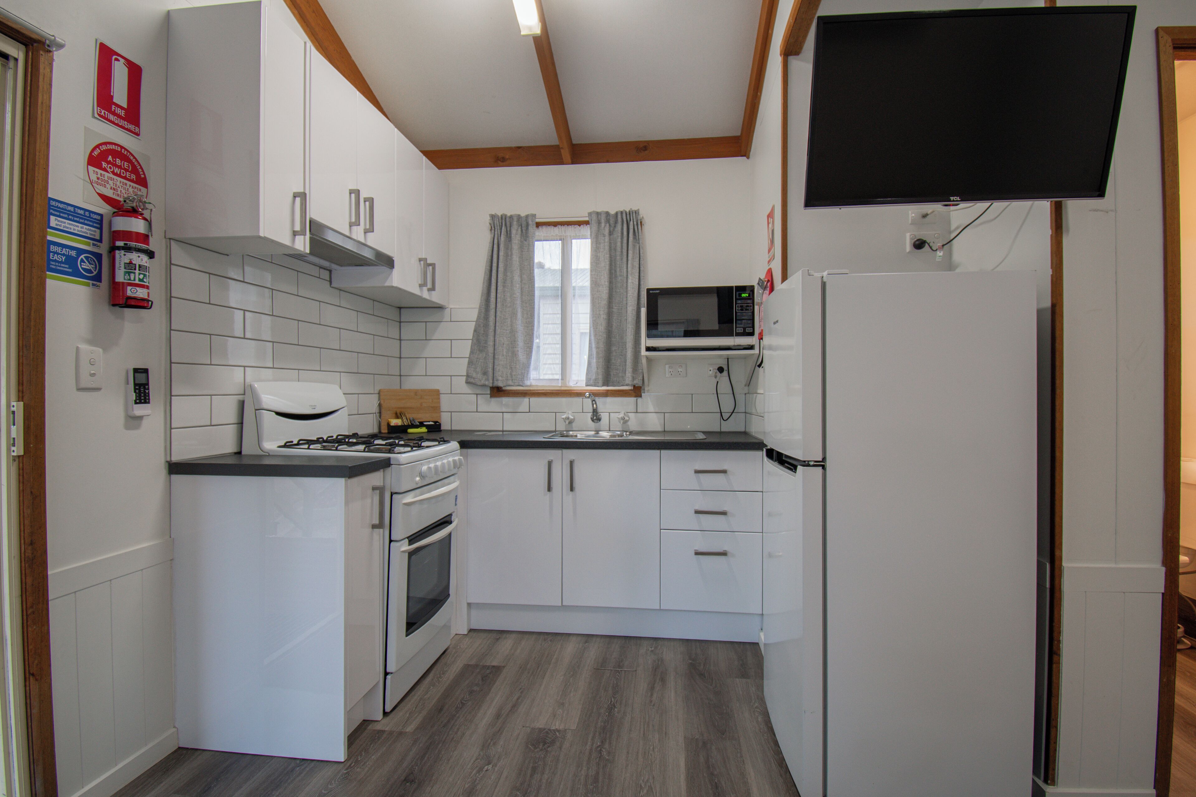 Eine kleine Küche mit weißen Schränken, einem Herd, Backofen, einer Mikrowelle und einem Kühlschrank.