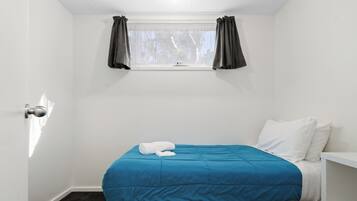 A small, single-bed room with a window, a white door, and a dark carpet.
