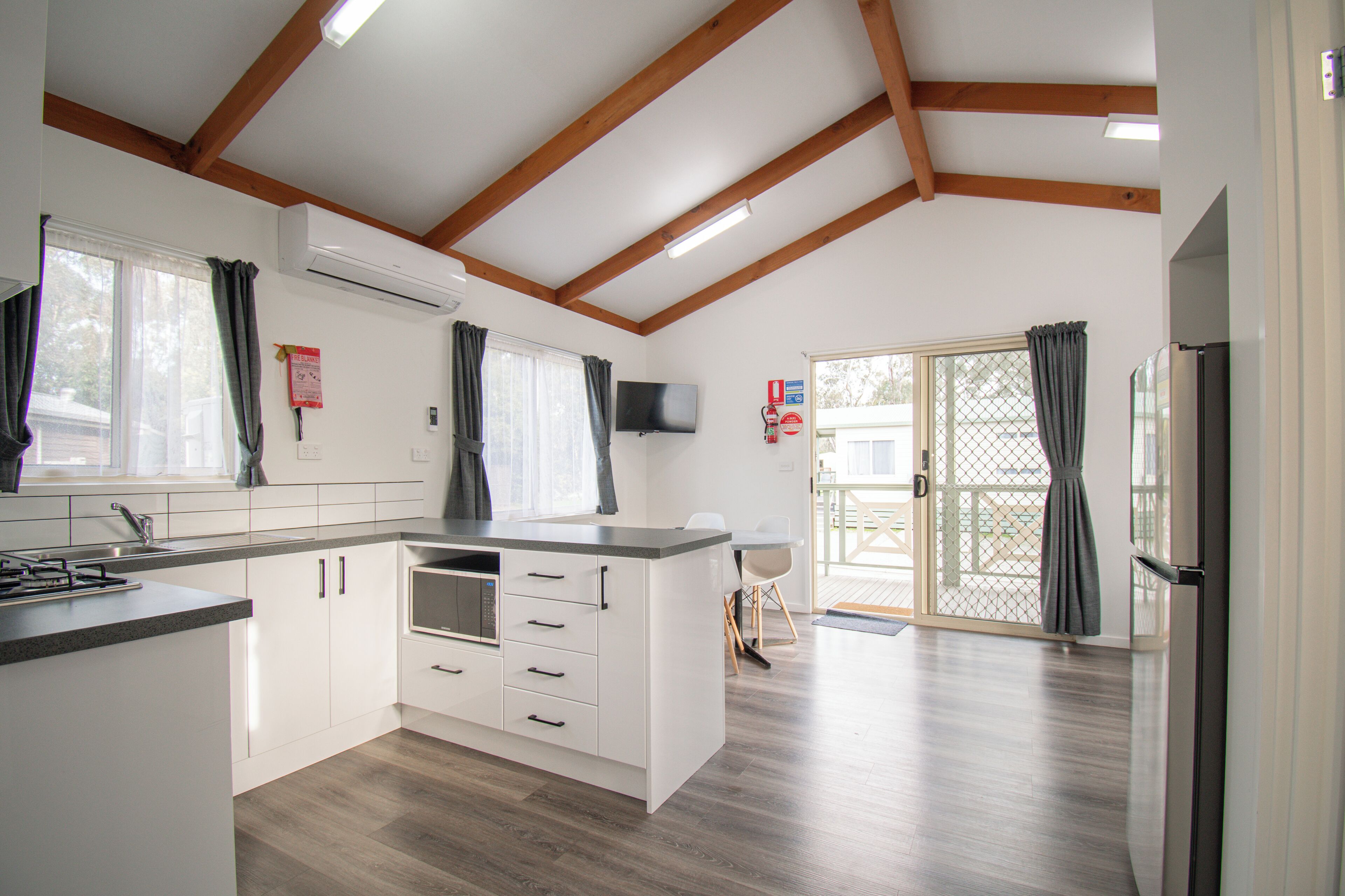 A modern kitchen with white cabinetry, a built-in microwave, and a large window with curtains.