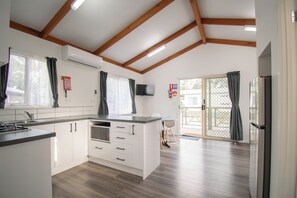 Une cuisine moderne avec des meubles blancs, un four à micro-ondes encastré et une grande fenêtre avec des rideaux.