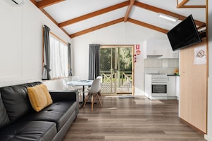 Un espacio habitable compacto con sofá, mesa de comedor, sillas, kitchenette y televisor montado en la pared.