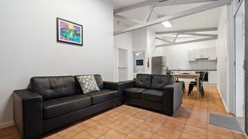 A modern living room with a black leather sofa, a small table, and a kitchen in the background.