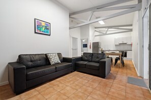 Een moderne woonkamer met een zwarte leren bank, een klein tafeltje en een keuken op de achtergrond.