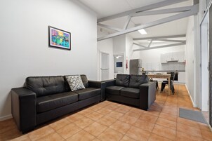 A modern living room with a black leather sofa, a small table, and a kitchen in the background.