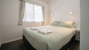 A bedroom with a bed, a window with curtains, a bedside table, and a wall-mounted light. - BIG4 Tiny Away Stay – Seymour Riverside (Seymour)