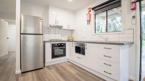 A modern kitchen with white cabinetry, stainless steel appliances, and a window overlooking greenery. - BIG4 Tiny Away Stay – Seymour Riverside (Seymour)