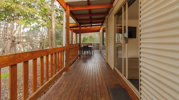 A wooden deck with a railing, a table and chairs, and a covered area with a metal roof. - BIG4 Tiny Away Stay – Seymour Riverside (Seymour)