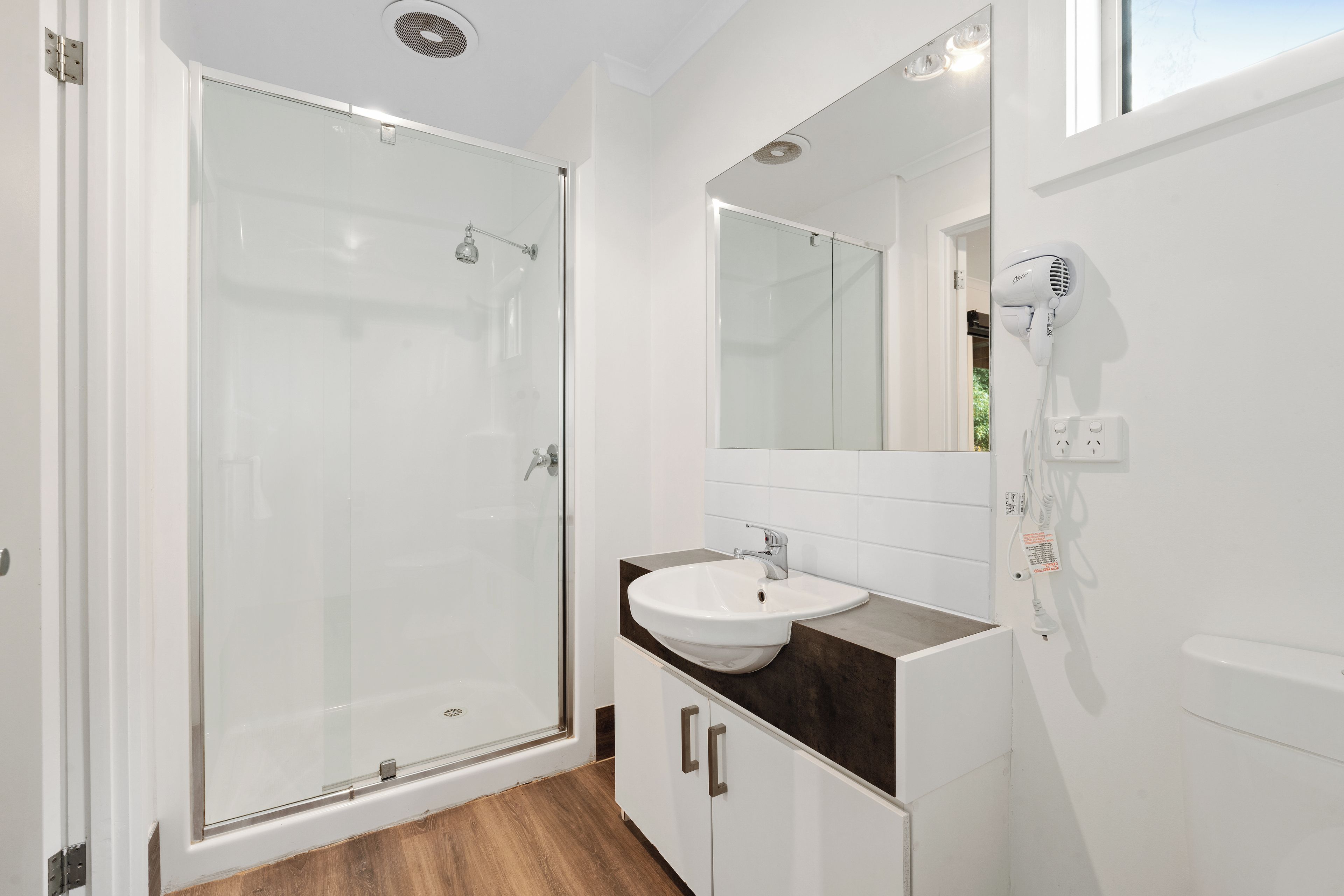 A modern bathroom with a glass shower enclosure, a white sink with a dark countertop, and a large mirror.