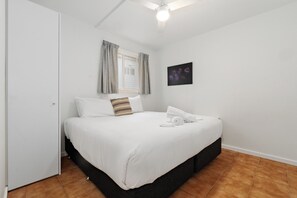 Une chambre à coucher avec un lit, une fenêtre avec des rideaux, un ventilateur de plafond et une œuvre d’art accrochée au mur.