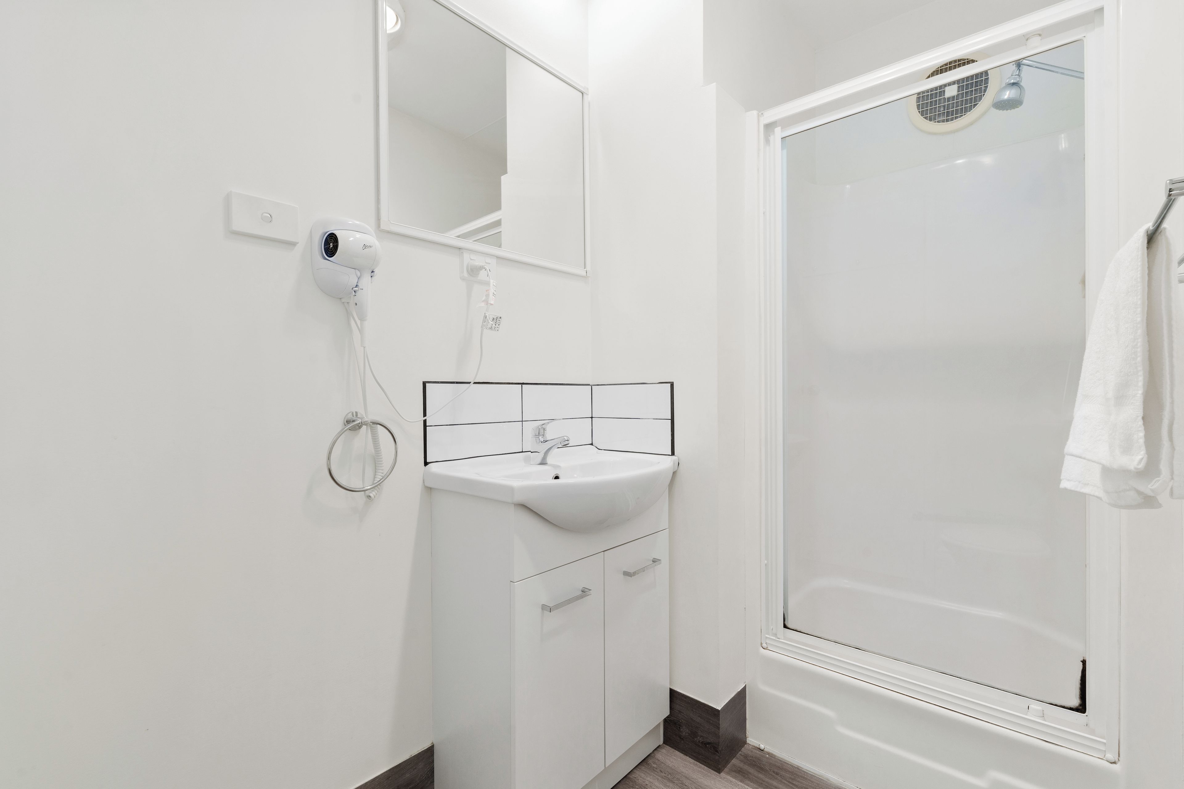 A modern bathroom with a white sink, mirror, and shower.