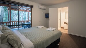 Une chambre à coucher avec un lit, une fenêtre donnant sur des arbres, un appareil de climatisation et une porte menant à la salle de bain.