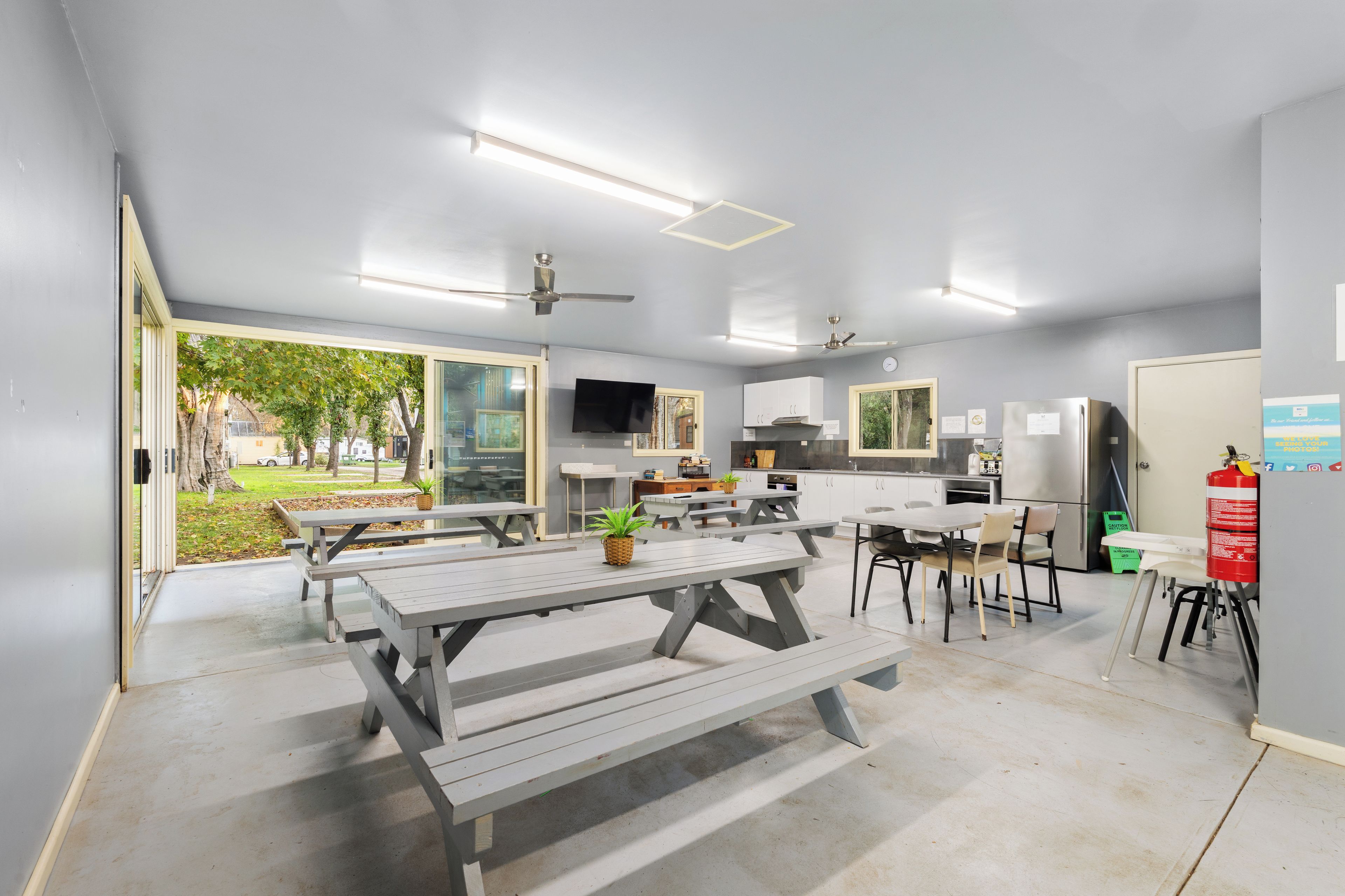 Una cocina moderna con electrodomésticos integrados, un comedor con mesas tipo picnic y un ventilador de techo.