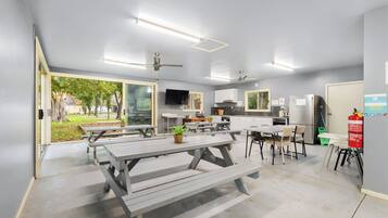Una cocina moderna con electrodomésticos integrados, un comedor con mesas tipo picnic y un ventilador de techo.