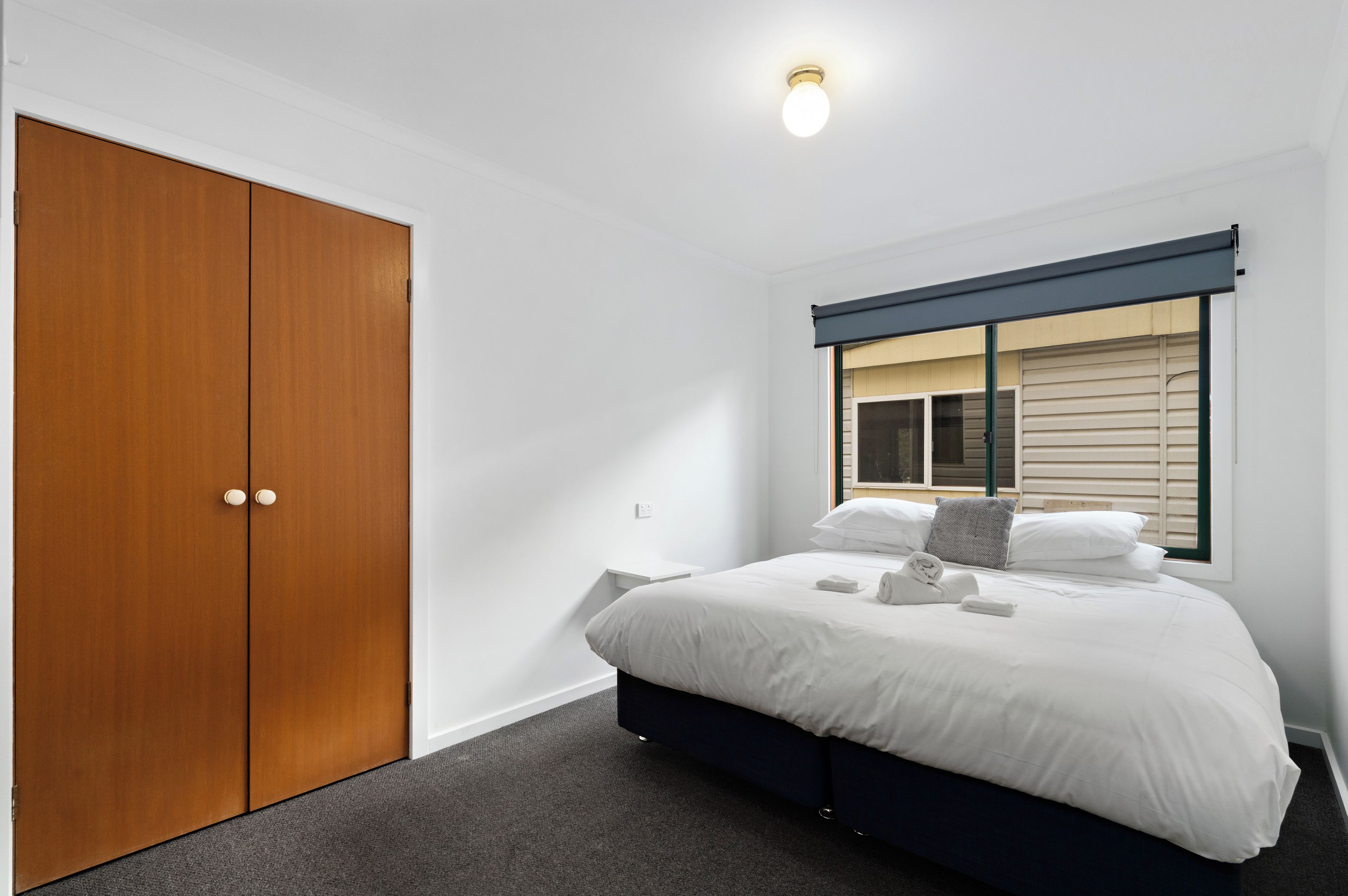 A bedroom with a bed, a wardrobe, a window with blinds, and a ceiling light.