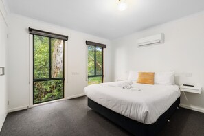 Een hotelkamer met een bed, nachtkastje, raam met uitzicht op bomen en een airconditioning.