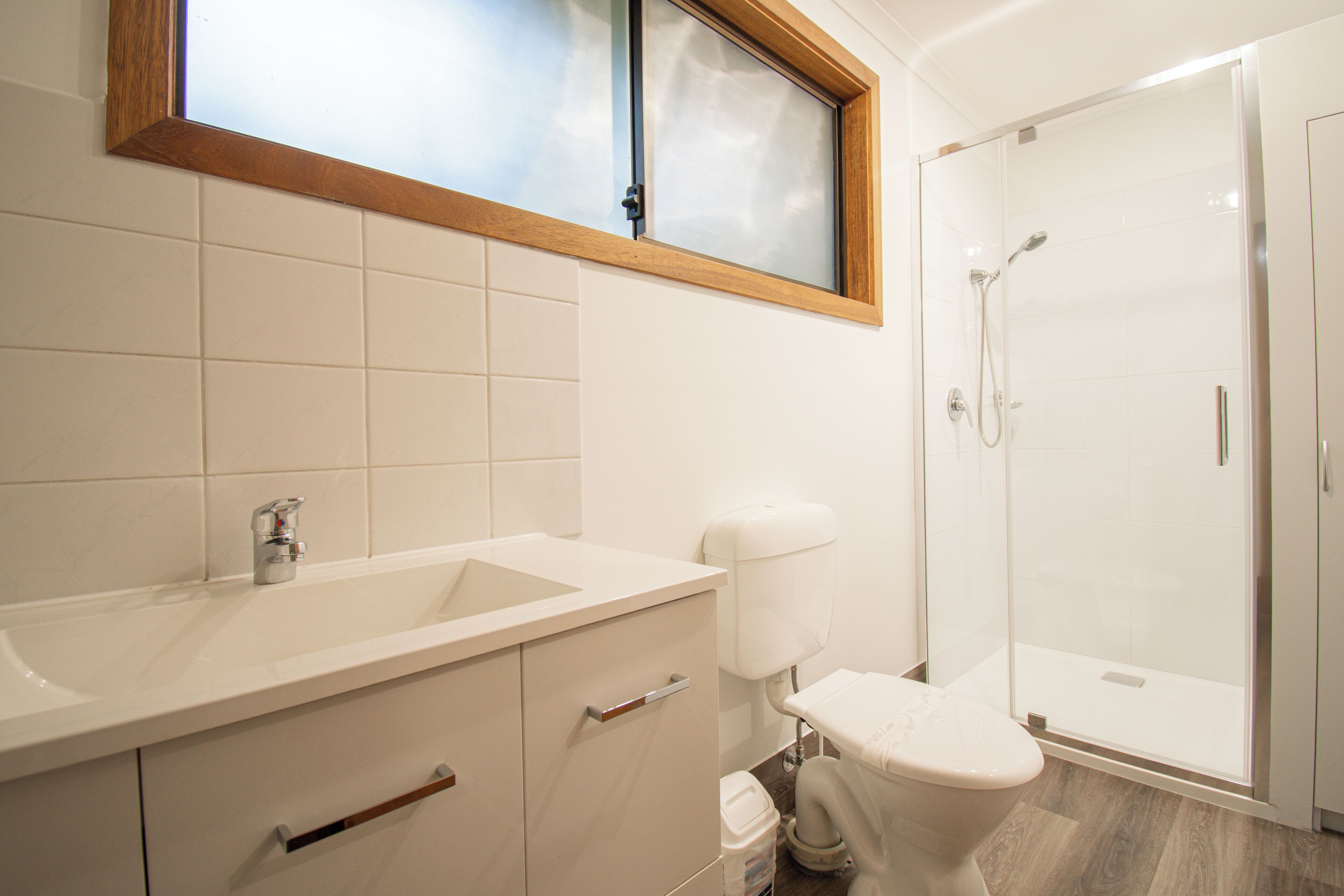 A bathroom with a shower, toilet, sink, and cabinets.