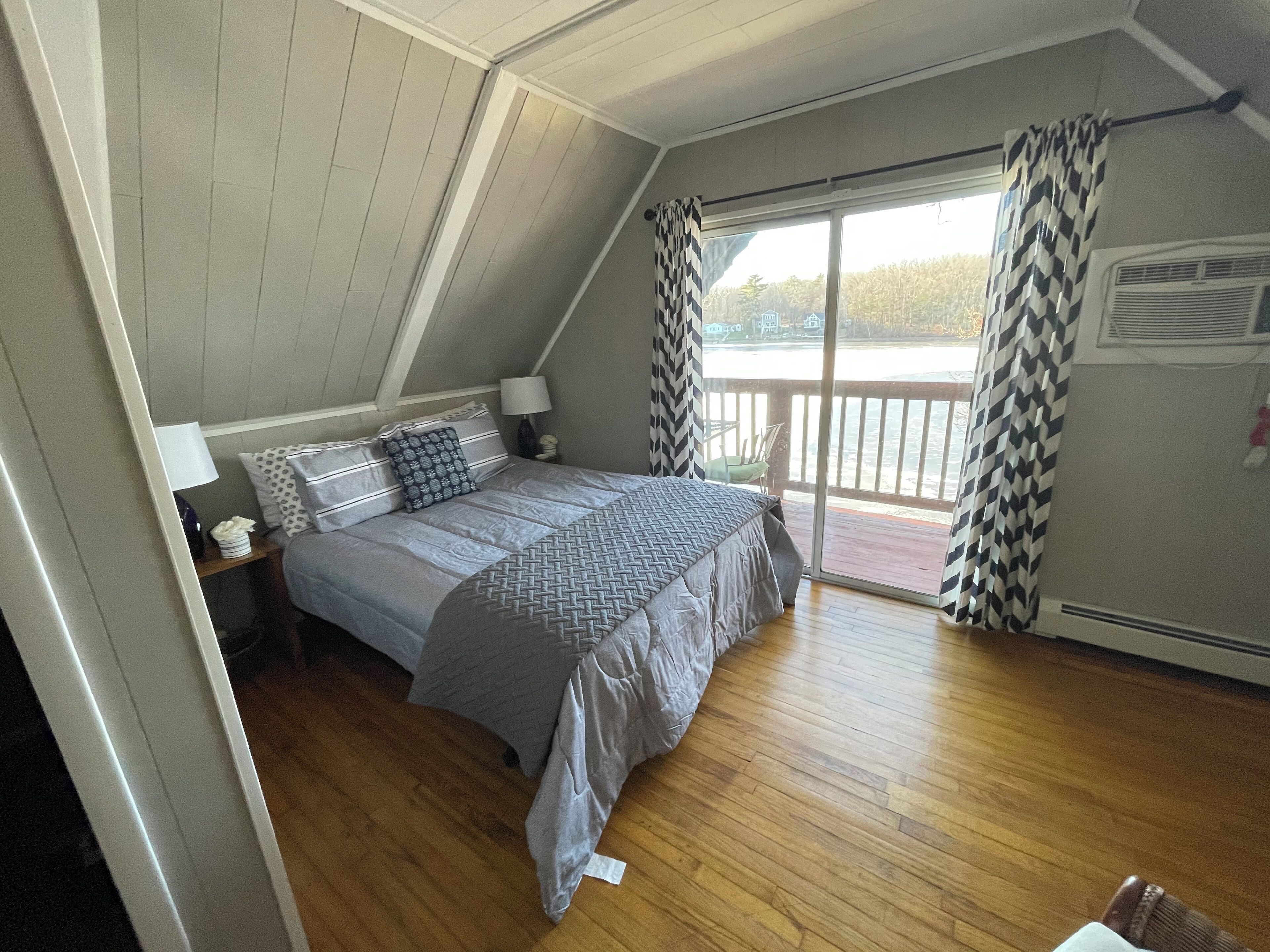 Ein Schlafzimmer mit Bett, Nachttisch, Lampe und Blick auf einen Balkon.