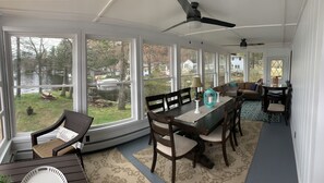 A sunroom with large windows, a dining table, chairs, a ceiling fan, and a view of a lake and houses. - Direct waterfront Lake House, stunning views Sleeps 8 on a private PENINSULA! (Sturbridge)