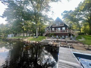 A lakeside cabin with a deck, a dock, and a small docked boat. - Direct waterfront Lake House, stunning views Sleeps 8 on a private PENINSULA! (Sturbridge)