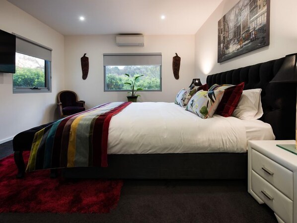 Une chambre moderne avec un grand lit, un tapis rouge, une table de chevet et une fenêtre donnant sur un paysage verdoyant.