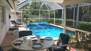 A covered outdoor area with a pool, lounge chairs, and a table set for dining.