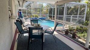 A covered patio area with a pool, outdoor seating, and a view of the surrounding greenery.