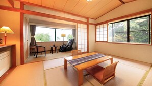 A traditional Japanese room with tatami flooring, a low wooden table, a chair, and a sliding door leading to a balcony with a view of greenery. - morinoakari (Hakone)